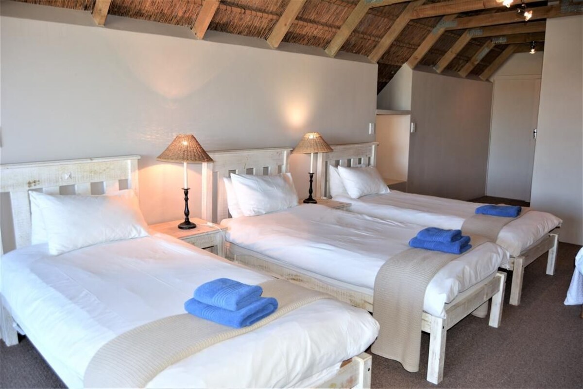 Una habitación con tres camas individuales, cada una con cabecero blanco y una lámpara en la mesita de noche.