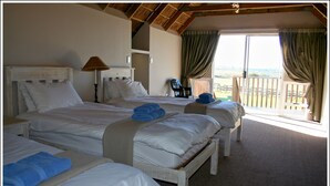 Quarto de hotel com duas camas, varanda e vista, e teto com vigas aparentes.