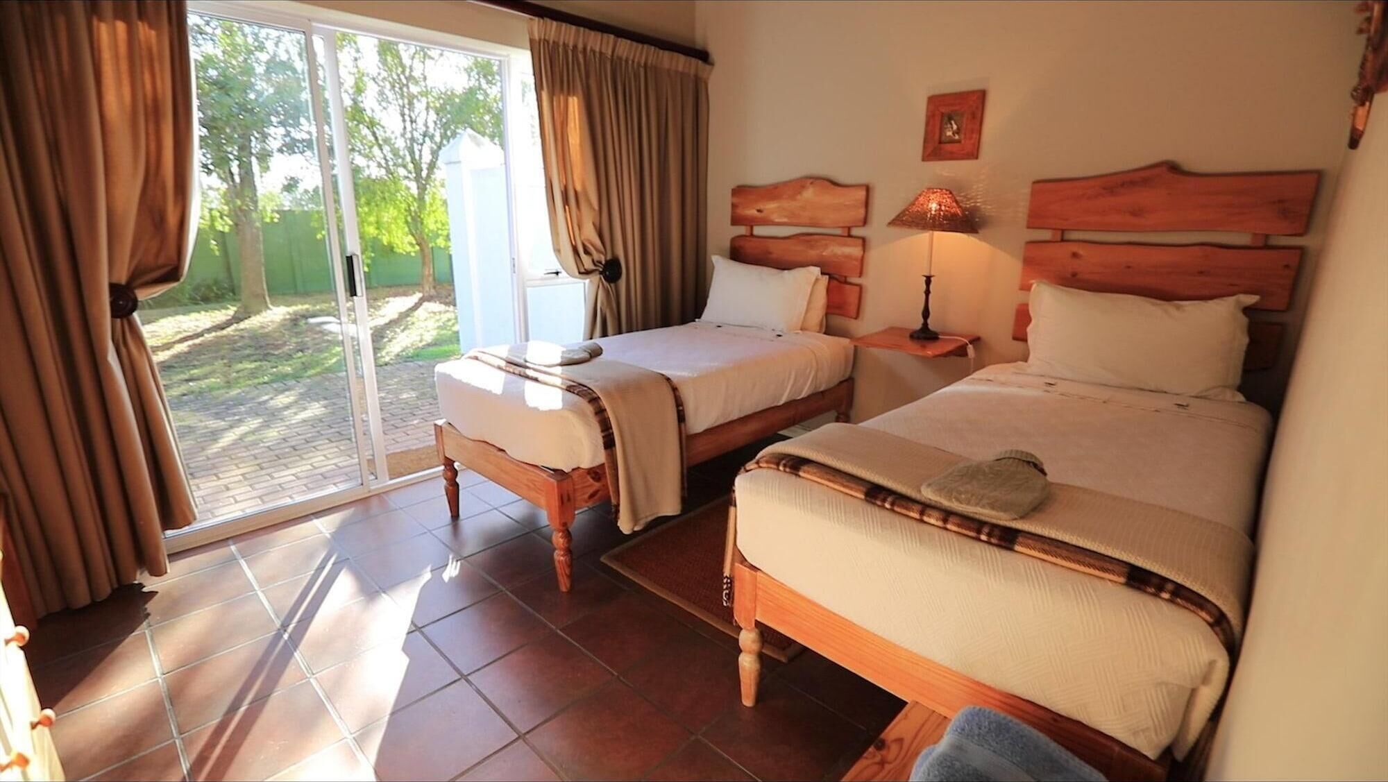 A bedroom with two beds, a sliding glass door to a garden, and a small table with a lamp.