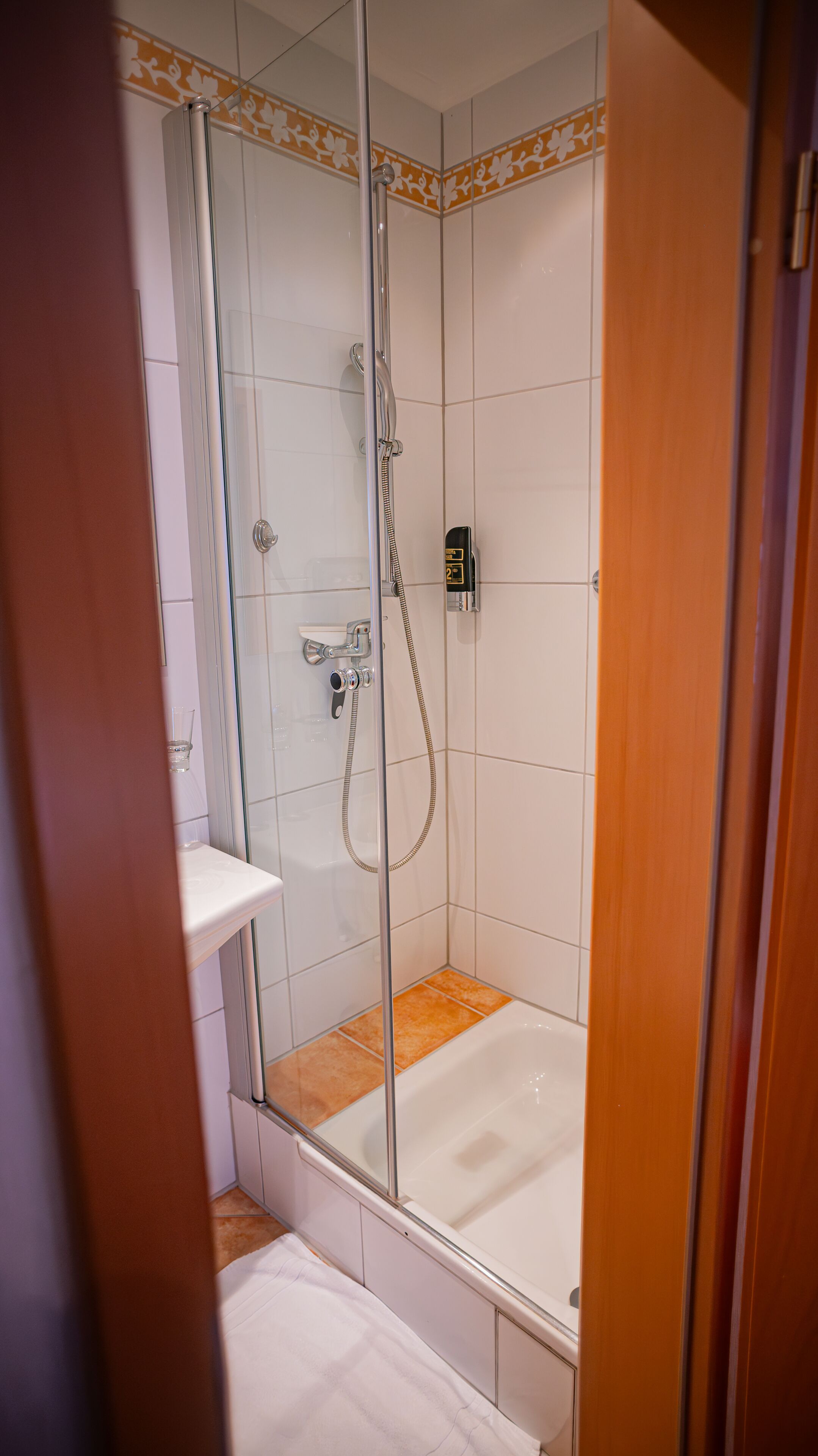 A glass-enclosed shower with a handheld showerhead and a control panel.