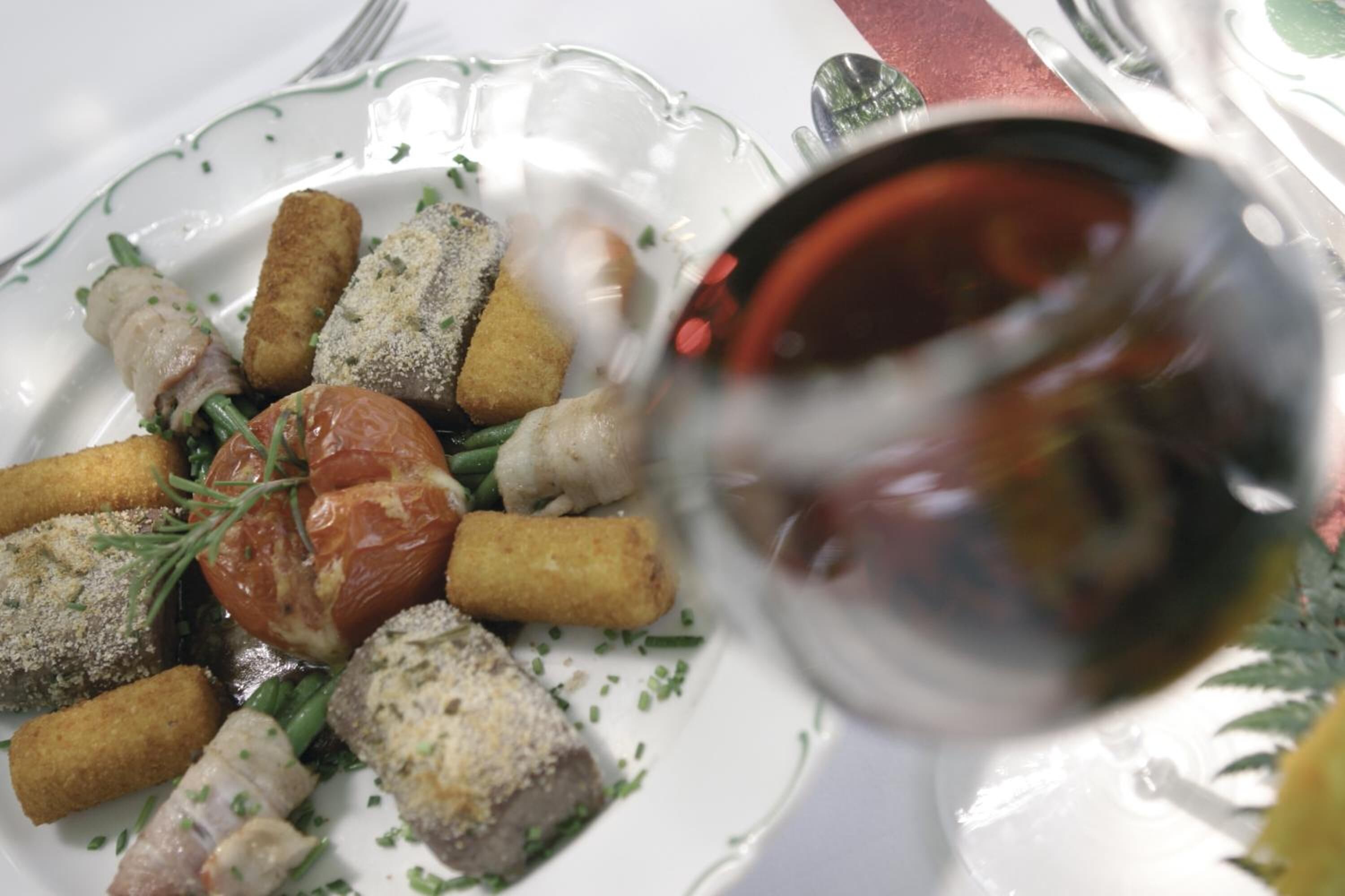 A plate of food with various items including breaded items and a tomato, accompanied by a glass of red wine.