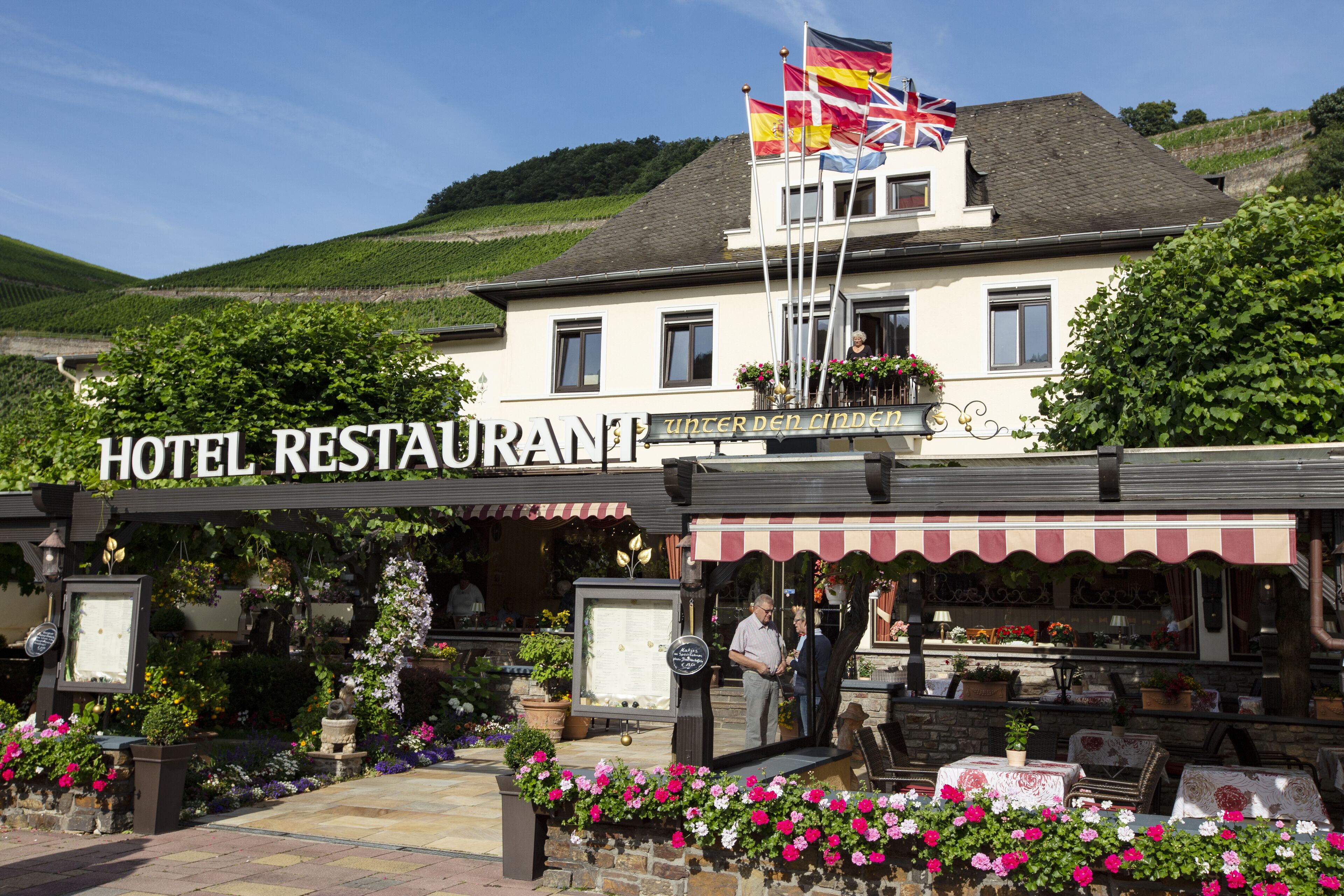 A hotel restaurant with outdoor seating, a signboard, and flags.