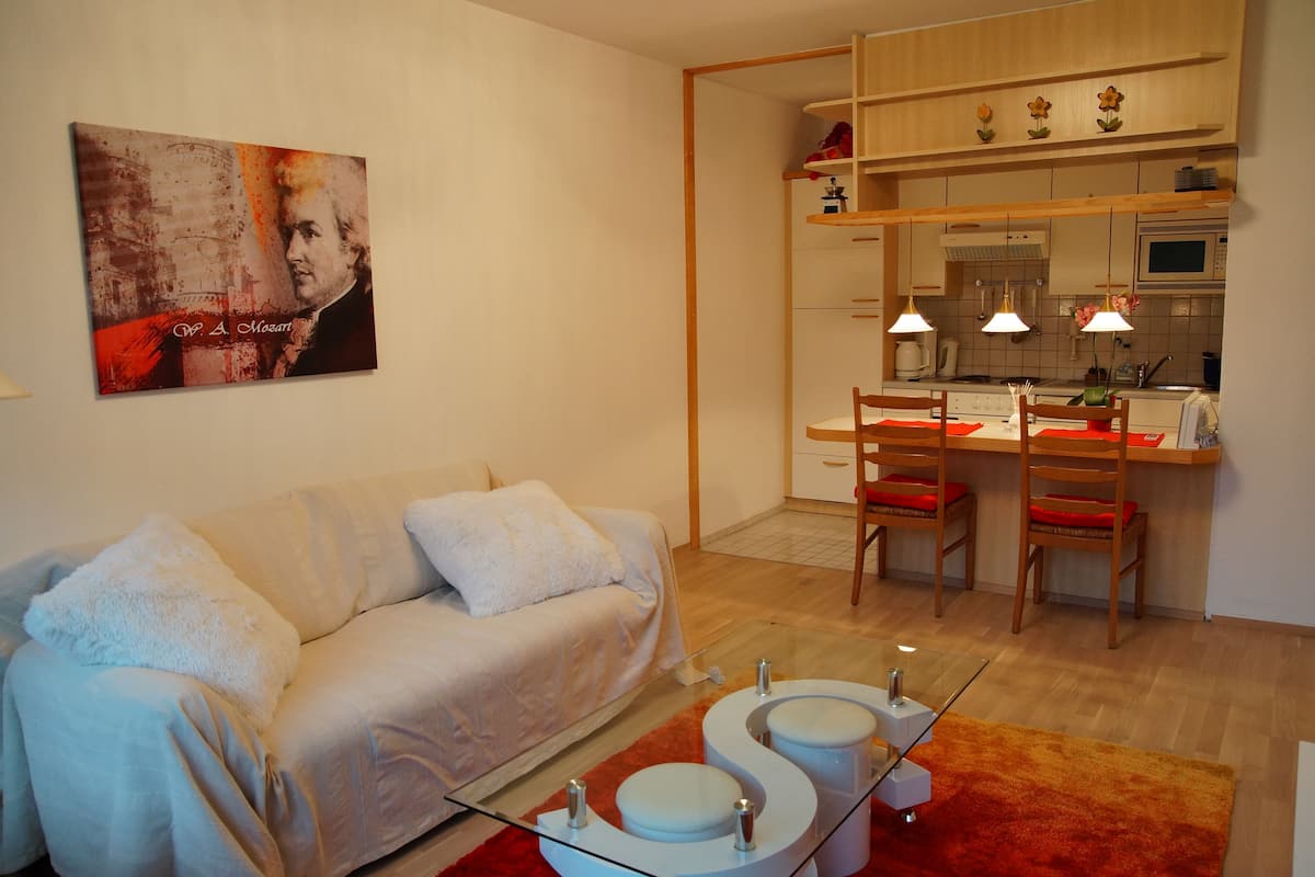 Un salon moderne avec un canapé, une table basse en verre et un coin cuisine comprenant une table à manger et des chaises.