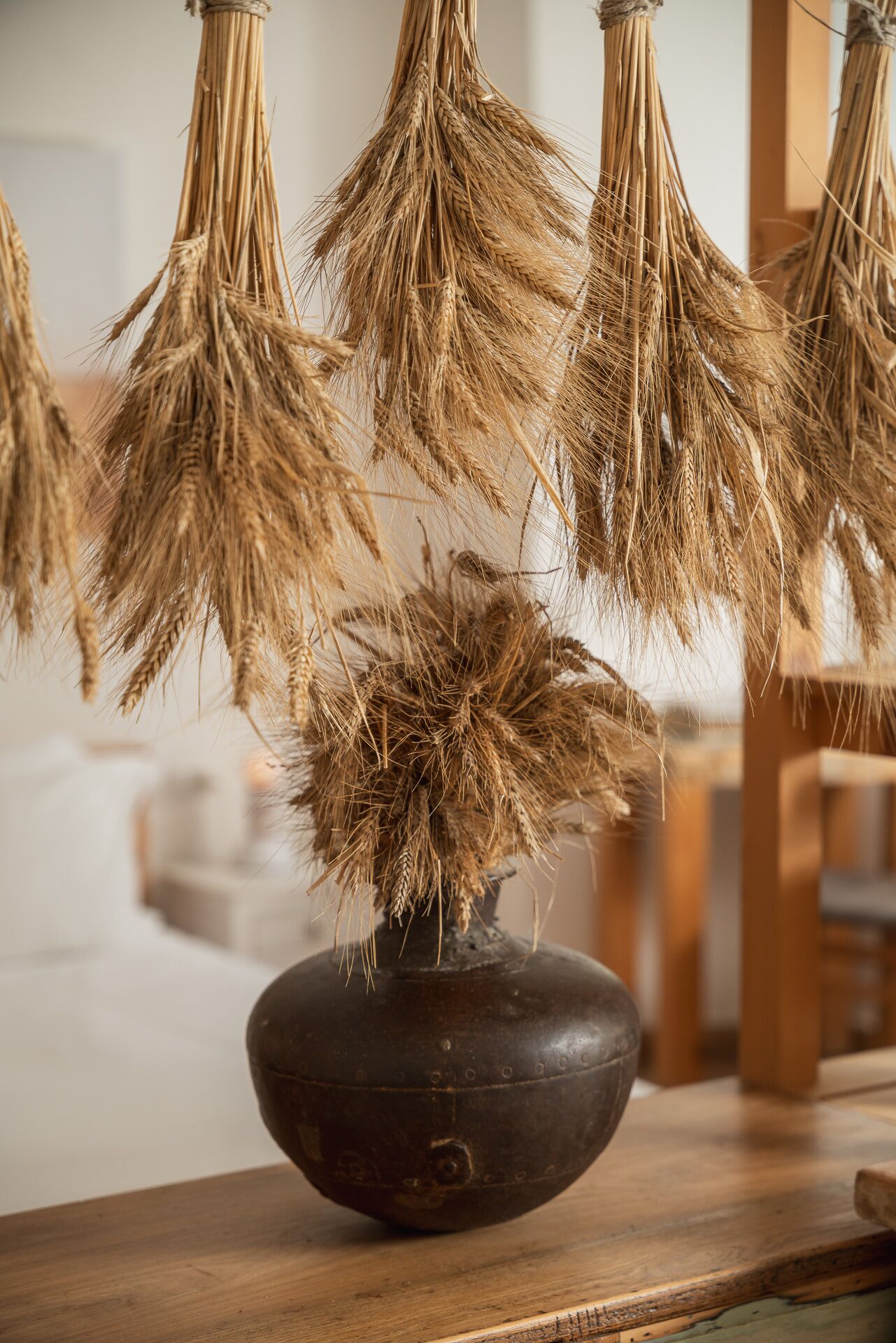 A dark wooden bowl with a rustic vase containing dried wheat stalks.