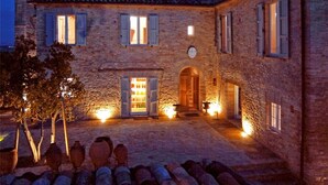 A stone building with a courtyard, featuring a central door and multiple windows with shutters.