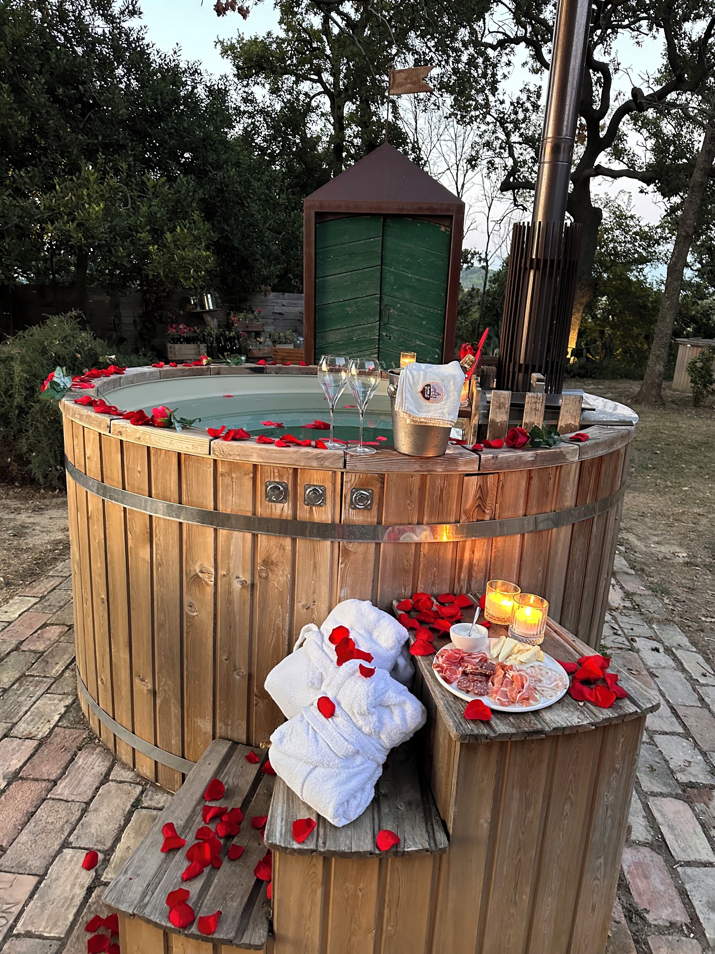 A wooden hot tub with rose petals, candles, and a bottle of champagne.
