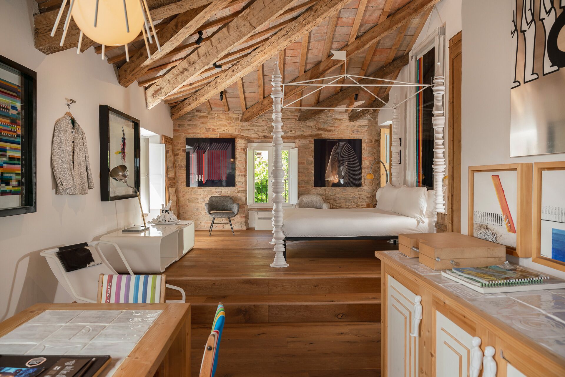 Une pièce avec un haut plafond en bois, un lit blanc, un bureau avec une chaise et un mur en pierre.