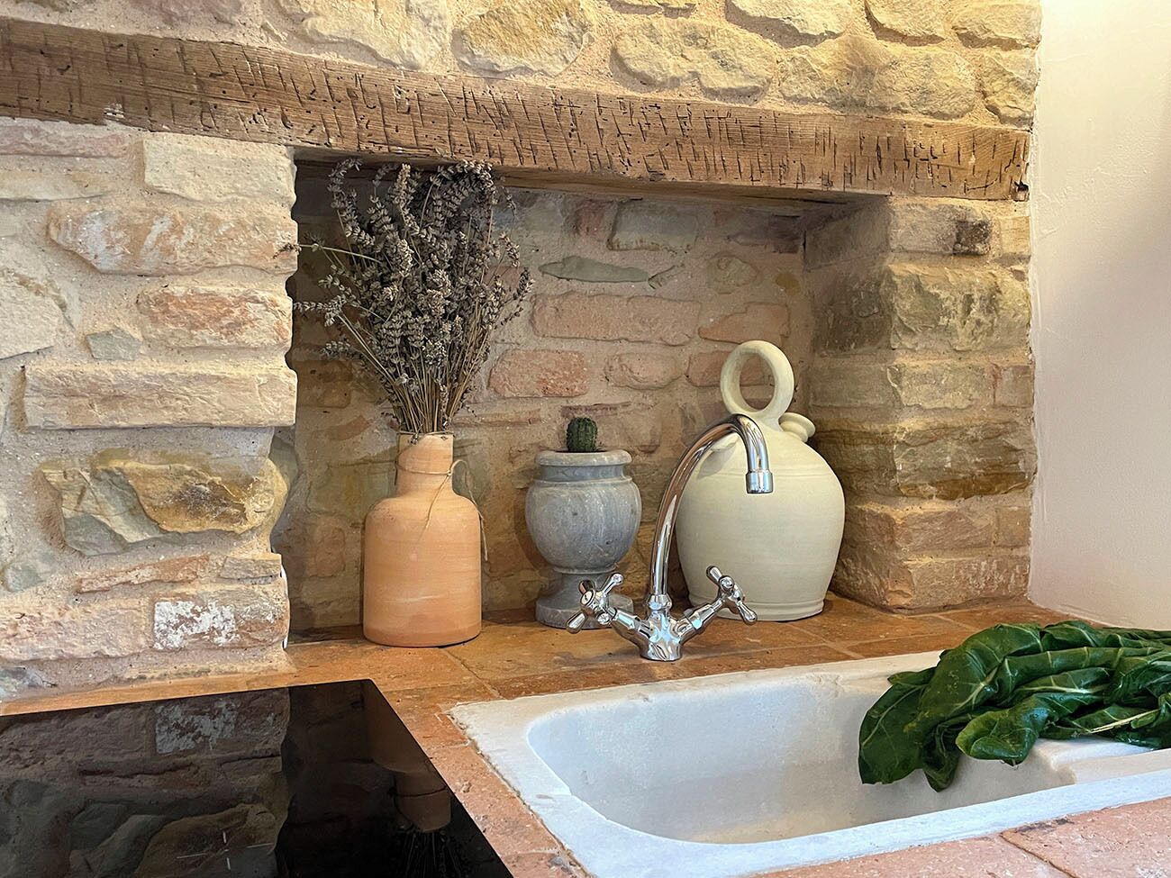 A stone fireplace with a built-in sink, a vase with dried flowers, and a potted plant.