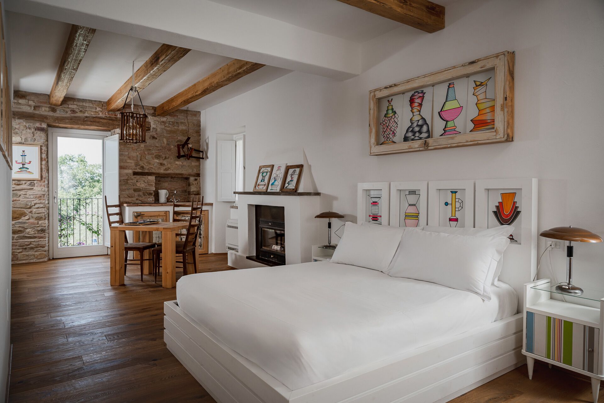 A bedroom with a bed, a fireplace, a dining area, and a stone wall.