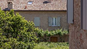 A rustic building with a tiled roof, a wooden door, and a small garden area with a blue vehicle parked in front.