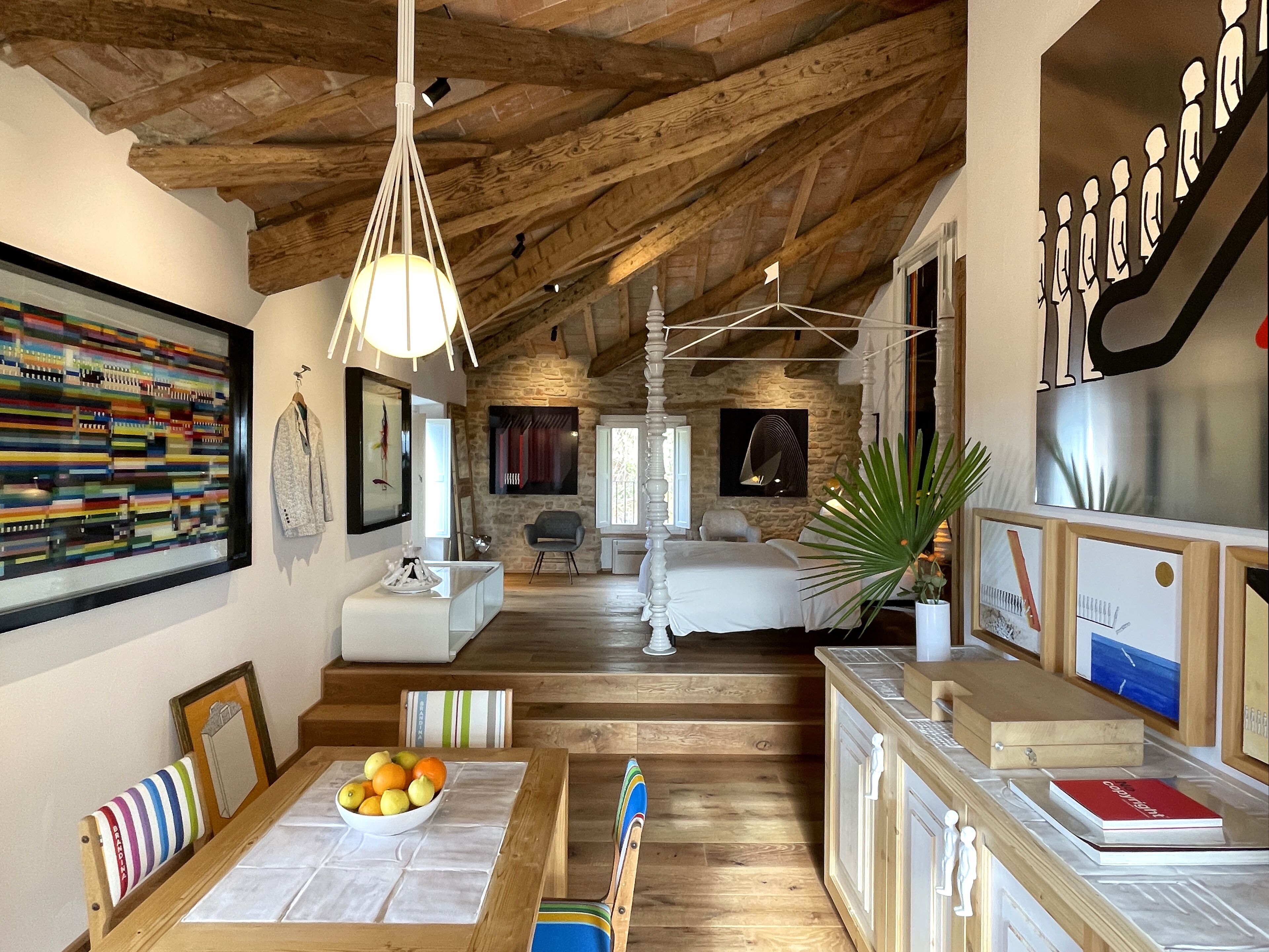 A spacious room with a high ceiling, wooden beams, a large window, and a bed.