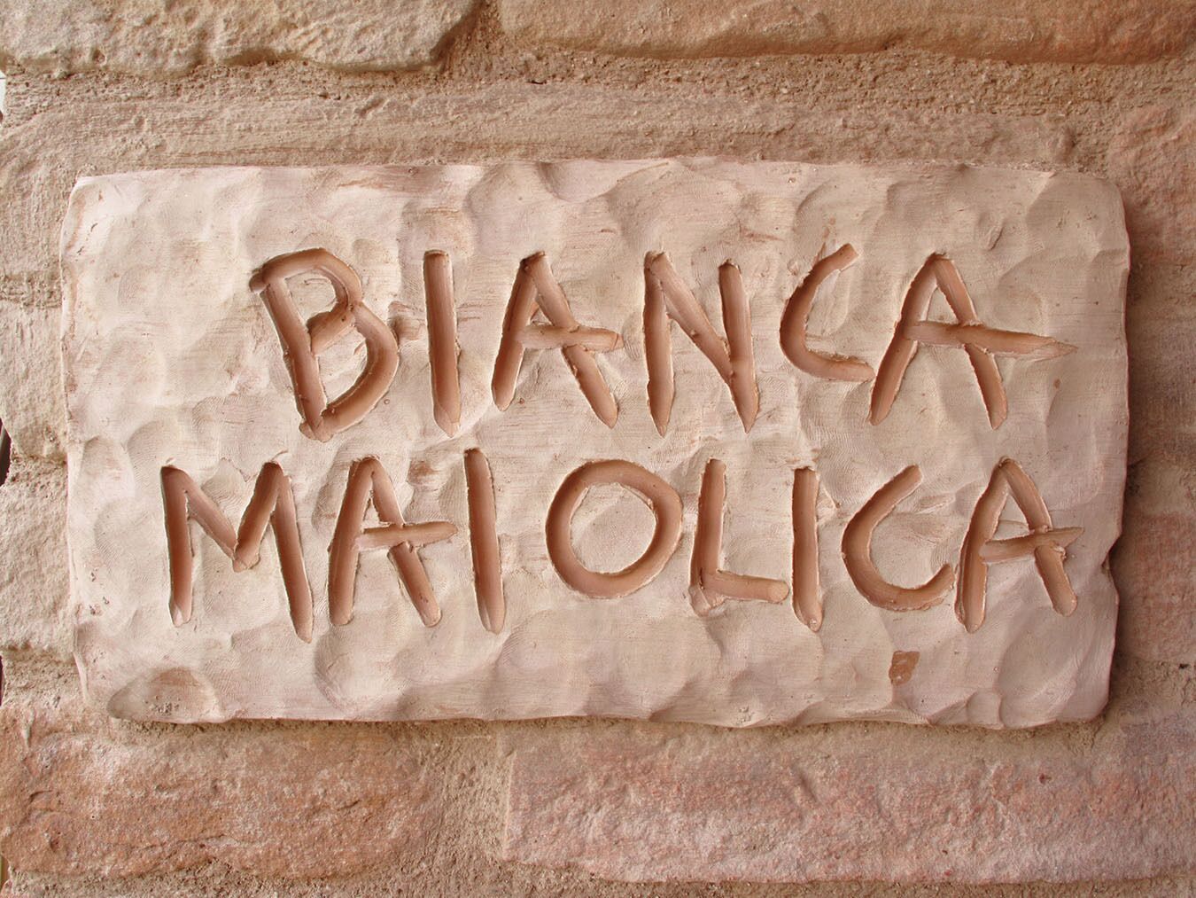 A stone plaque with the inscription "BIANCA MAJOLICA" on a brick wall.