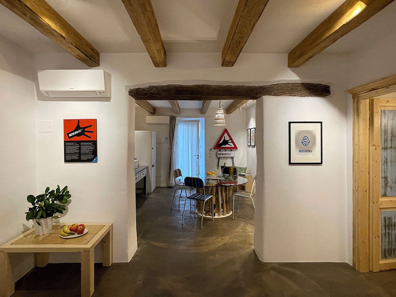 A hallway with a wooden ceiling, a table with apples and a plant, and a dining area with chairs and a table.