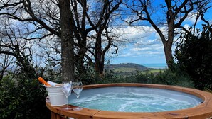 A hot tub with a wooden frame, a bucket, and two wine glasses on a wooden bench.