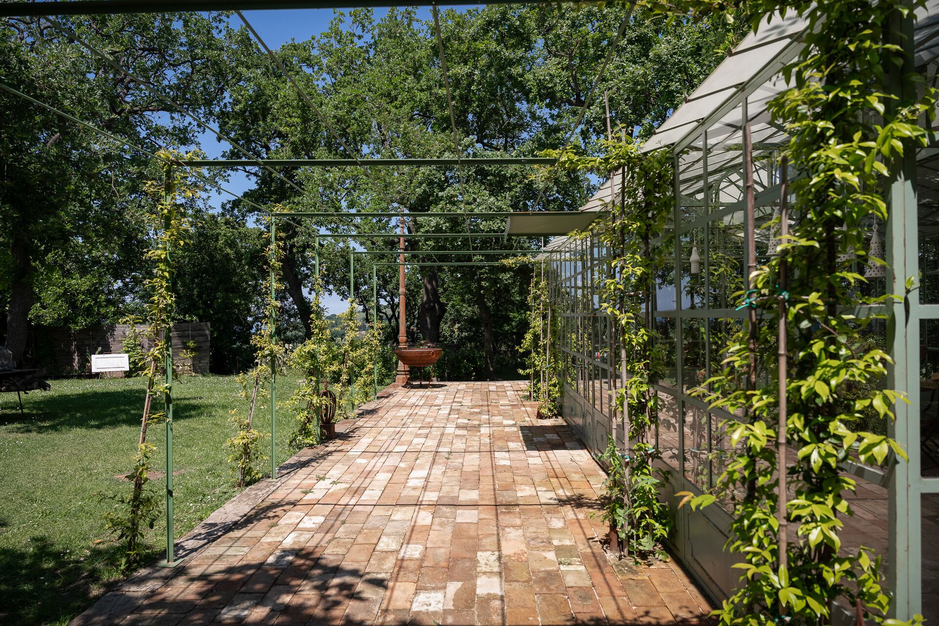 A brick pathway leading to a greenhouse structure with a metal frame and glass panels.