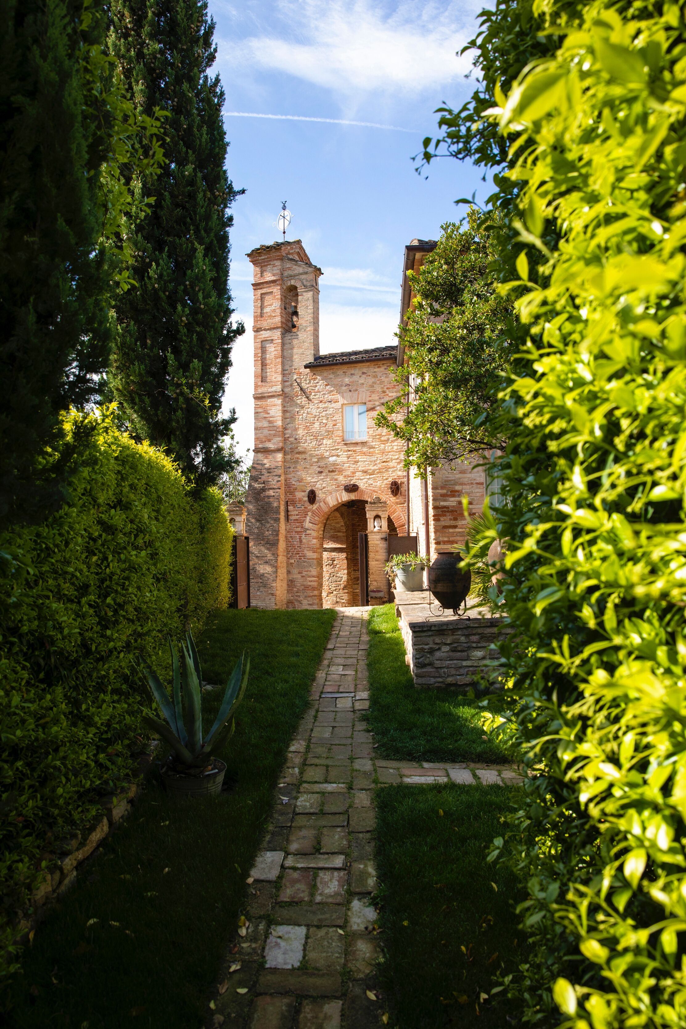 Un bâtiment en pierre doté d’une tour, entouré de verdure et bordé d’un chemin pavé.