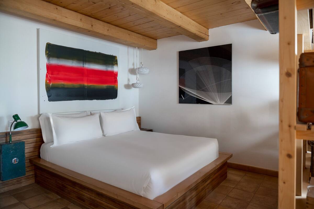 Ein Schlafzimmer mit einem Bett, einer Wandlampe und zwei Kunstwerken.