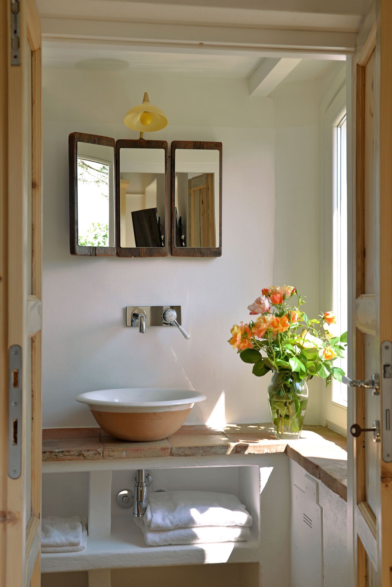 A bathroom with a white sink, a mirror, and a vase with flowers.