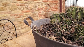 Una maceta metálica con una planta de cactus sobre una mesa de madera frente a una pared de piedra.