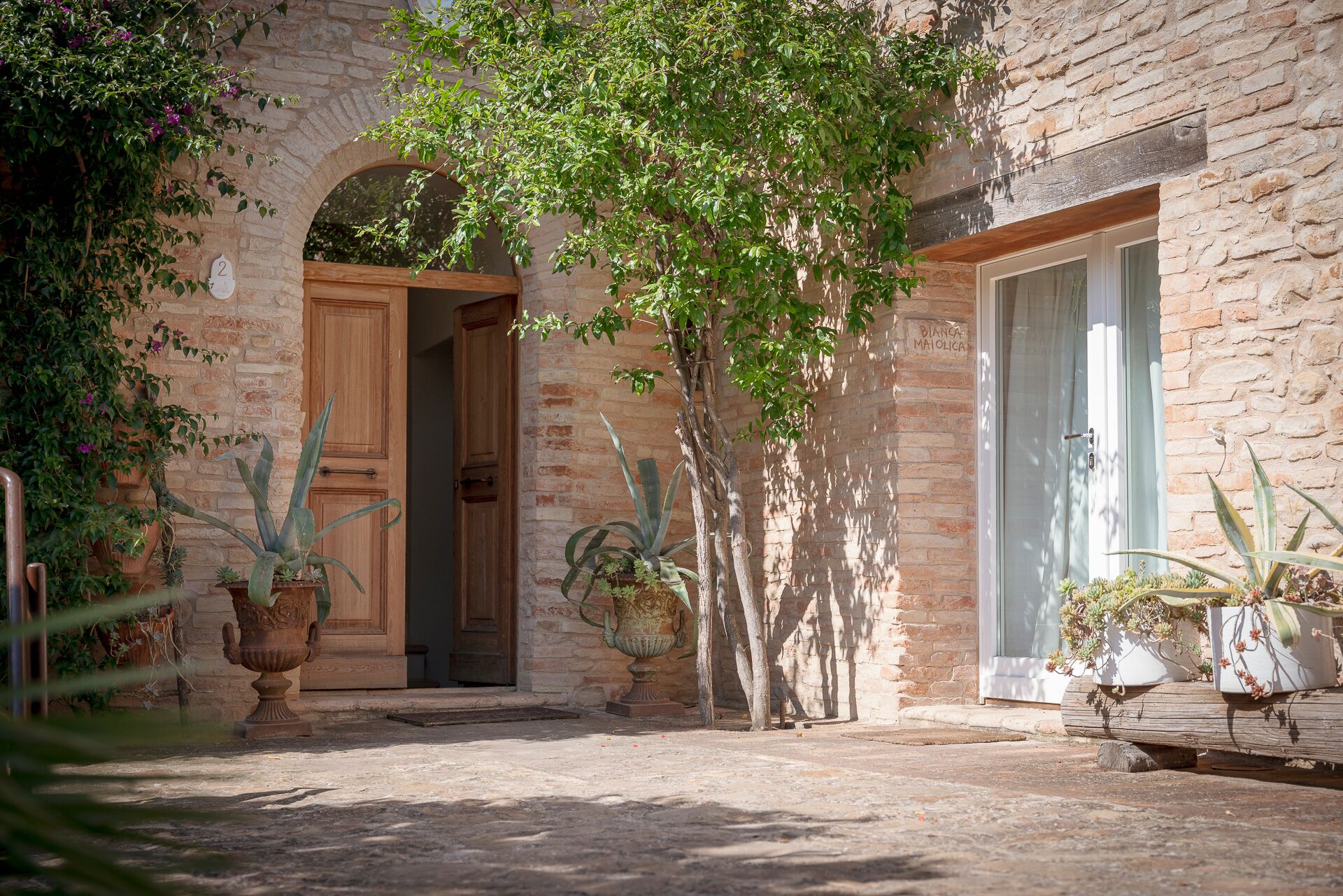 Un edificio in pietra rustica con una porta in legno e una finestra, circondato da piante in vaso e un piccolo giardino.