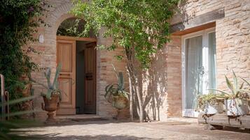 Un edificio in pietra rustica con una porta in legno e una finestra, circondato da piante in vaso e un piccolo giardino.