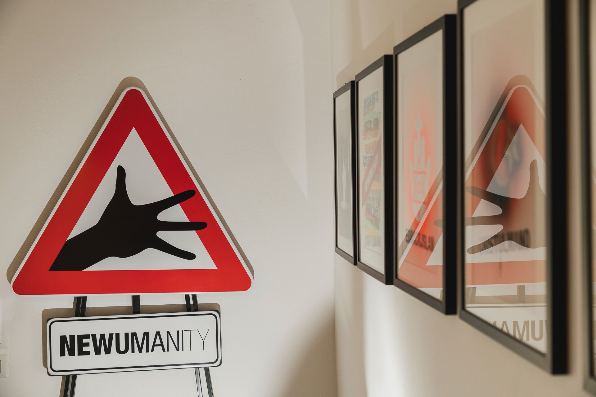 A triangular warning sign with a hand symbol and the word 'NEWUMANITY' below it.
