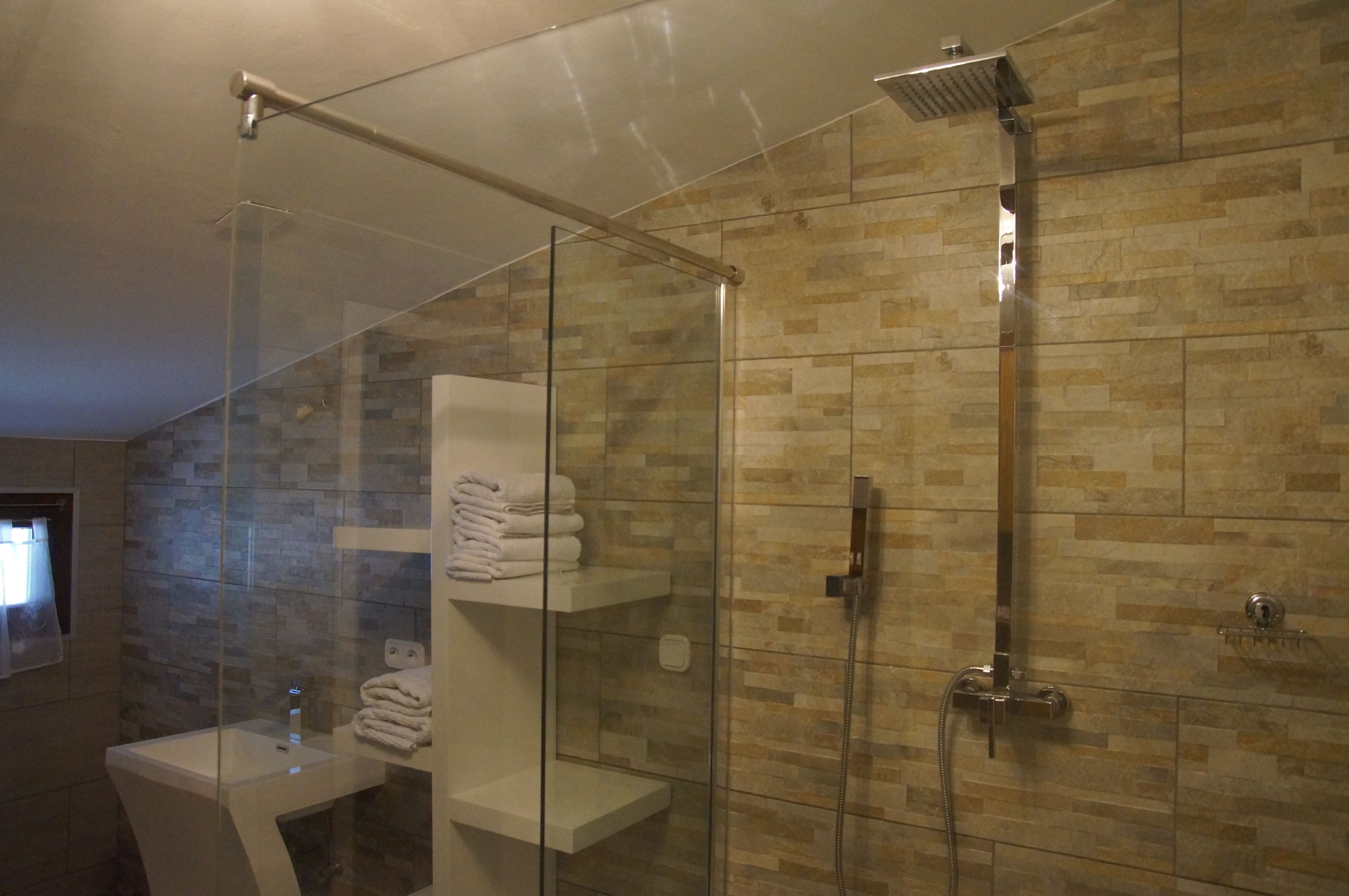 Ducha con cerramiento de vidrio, cabezal de ducha de mano y grifo empotrado.