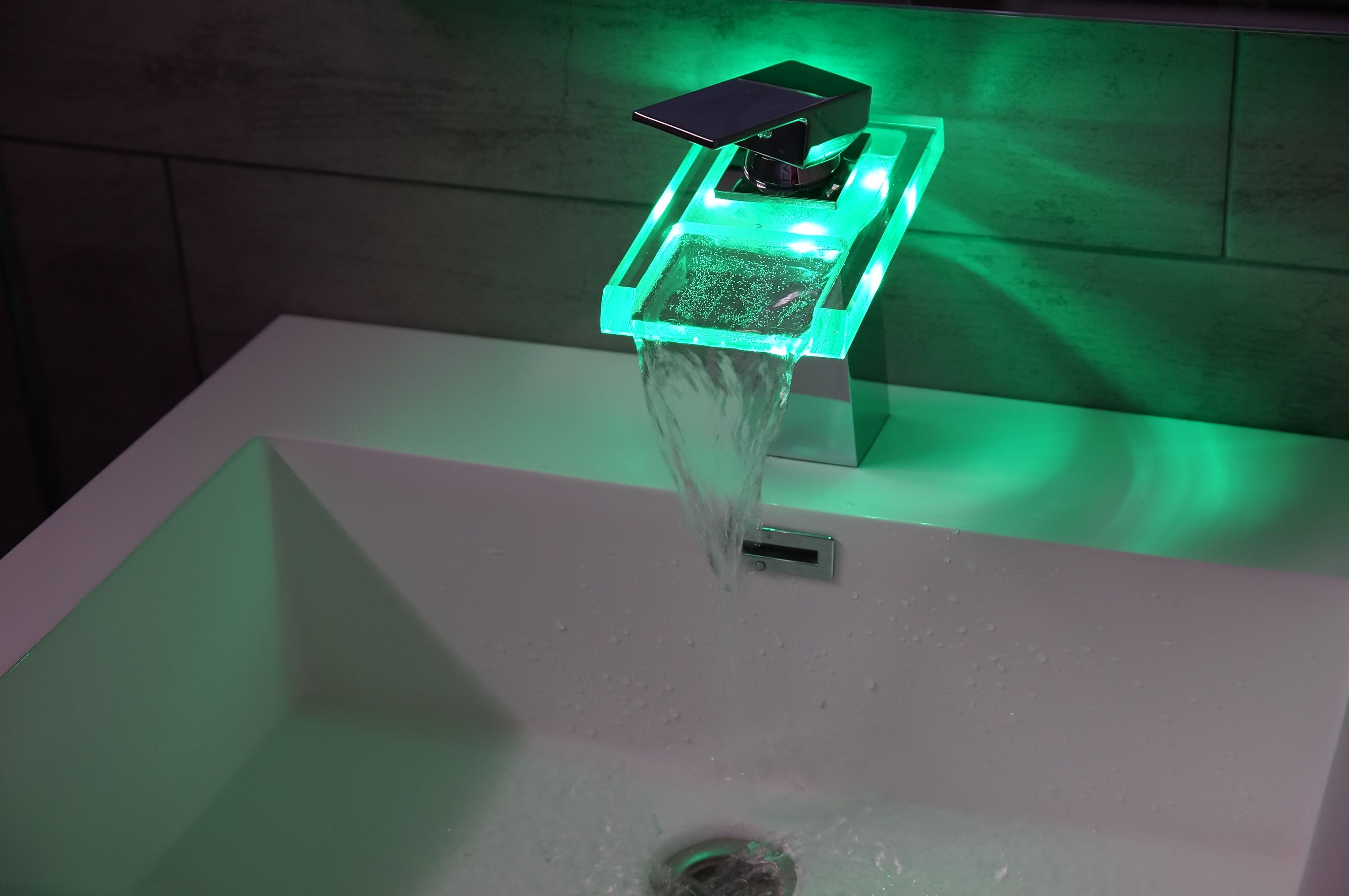 A modern bathroom with a square sink and a green-lit faucet.