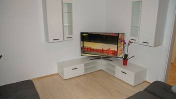 Una sala de estar moderna con un televisor de pantalla plana, muebles blancos y una pequeña planta en maceta.