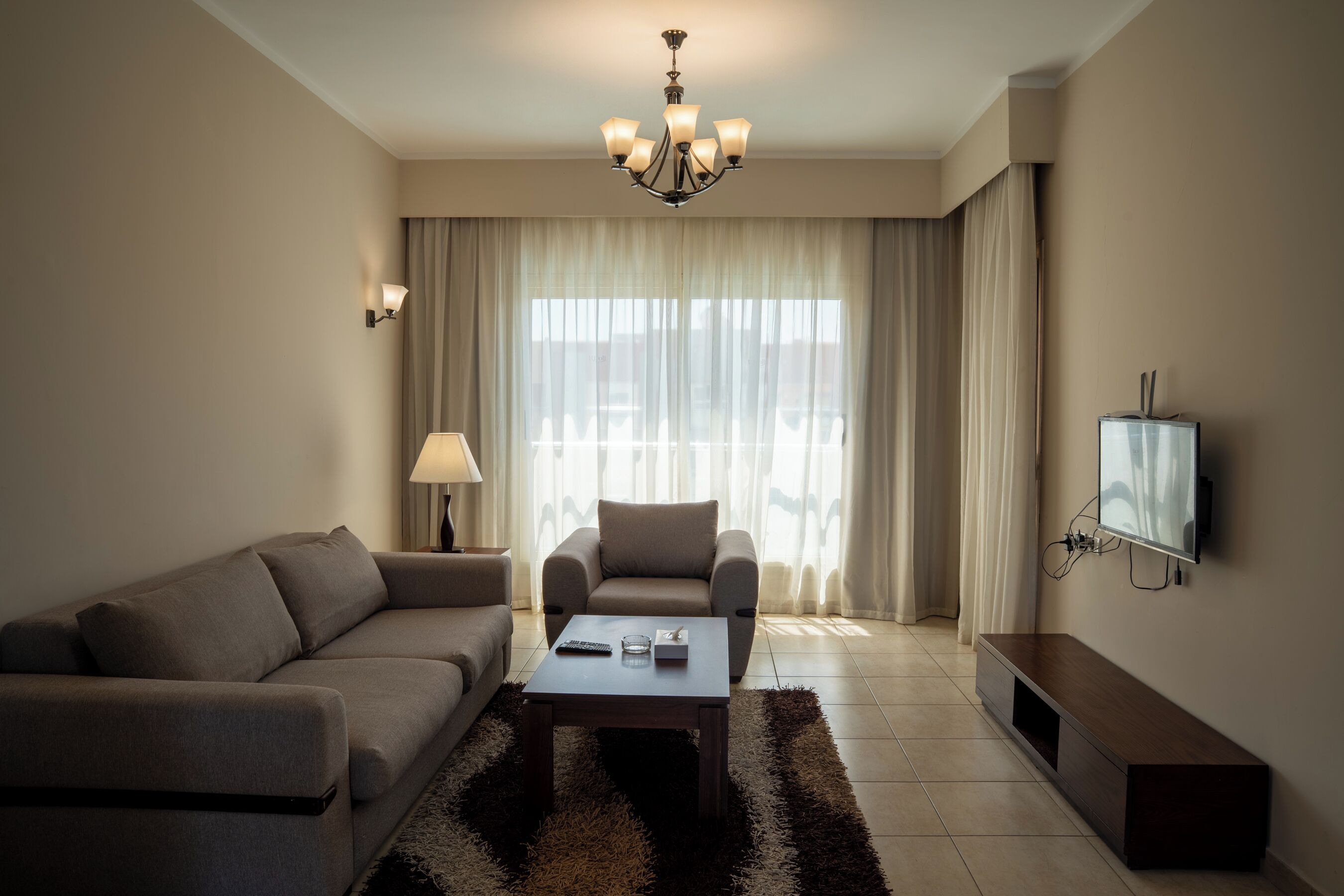 Ein modernes Wohnzimmer mit Sofa, Sessel, Couchtisch, Fernseher und einer Chandelier.