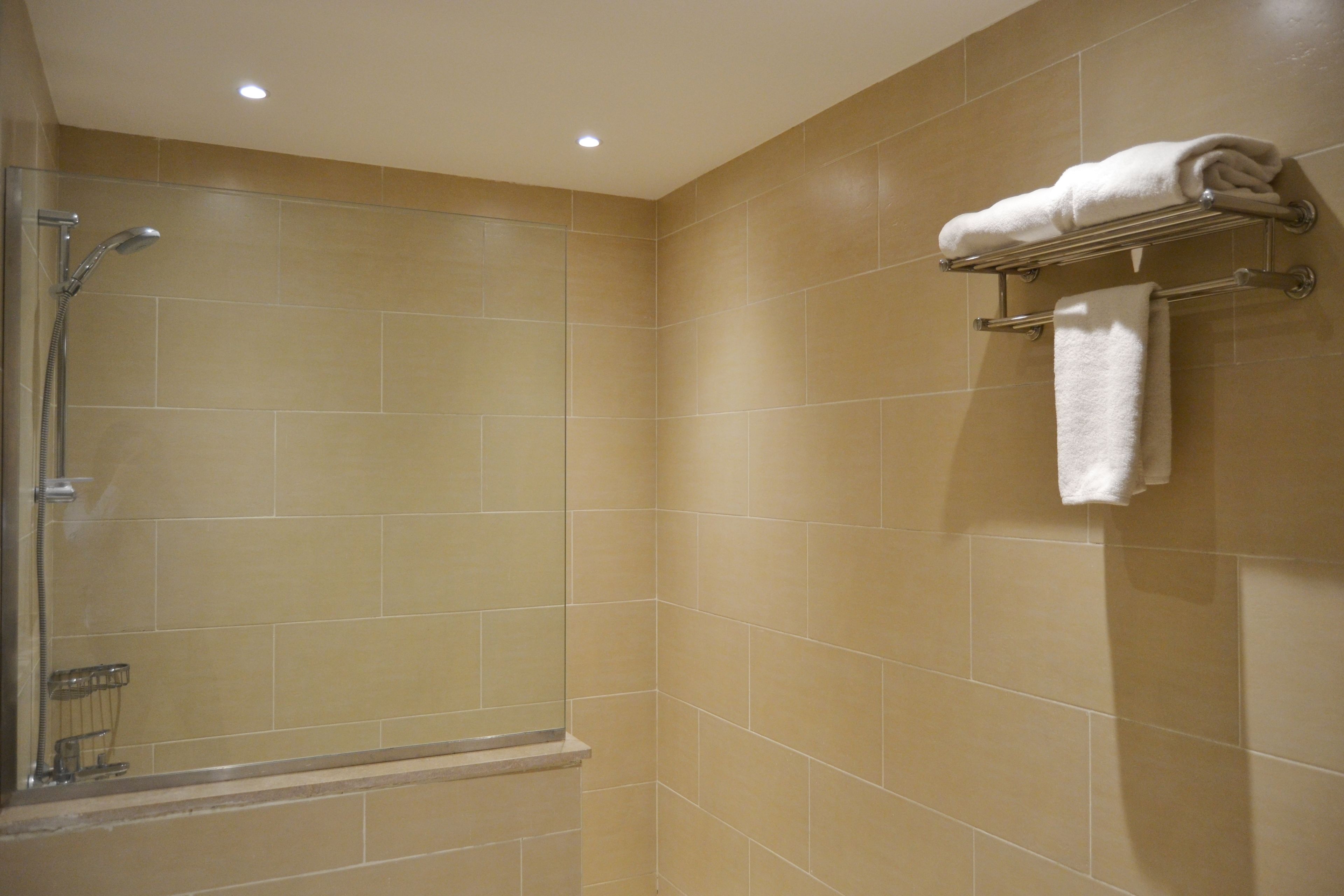 A bathroom with beige tiles, a shower, and a towel rack with towels.