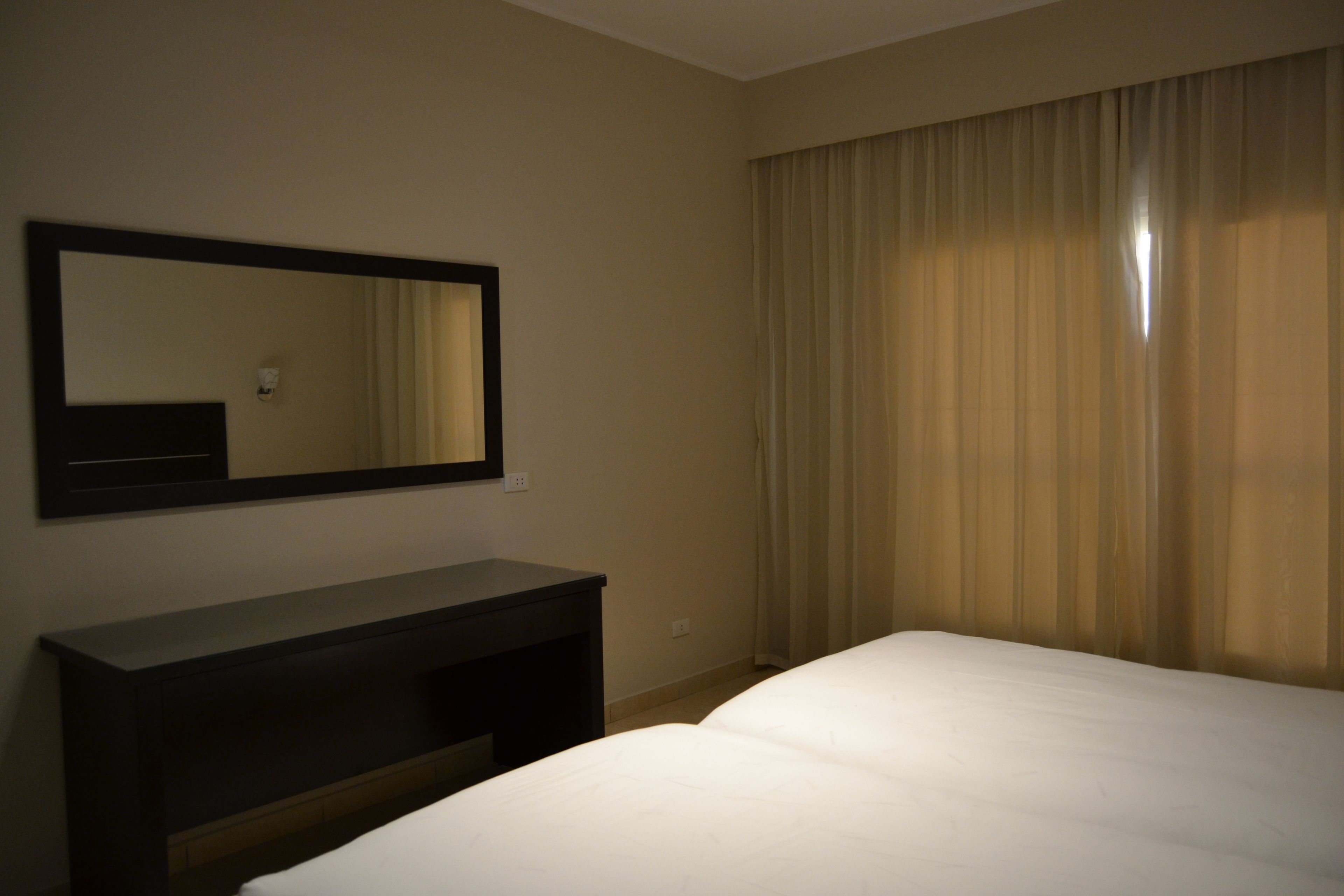 Een hotelkamer met een bed, een donker bureau en een grote spiegel aan de muur.