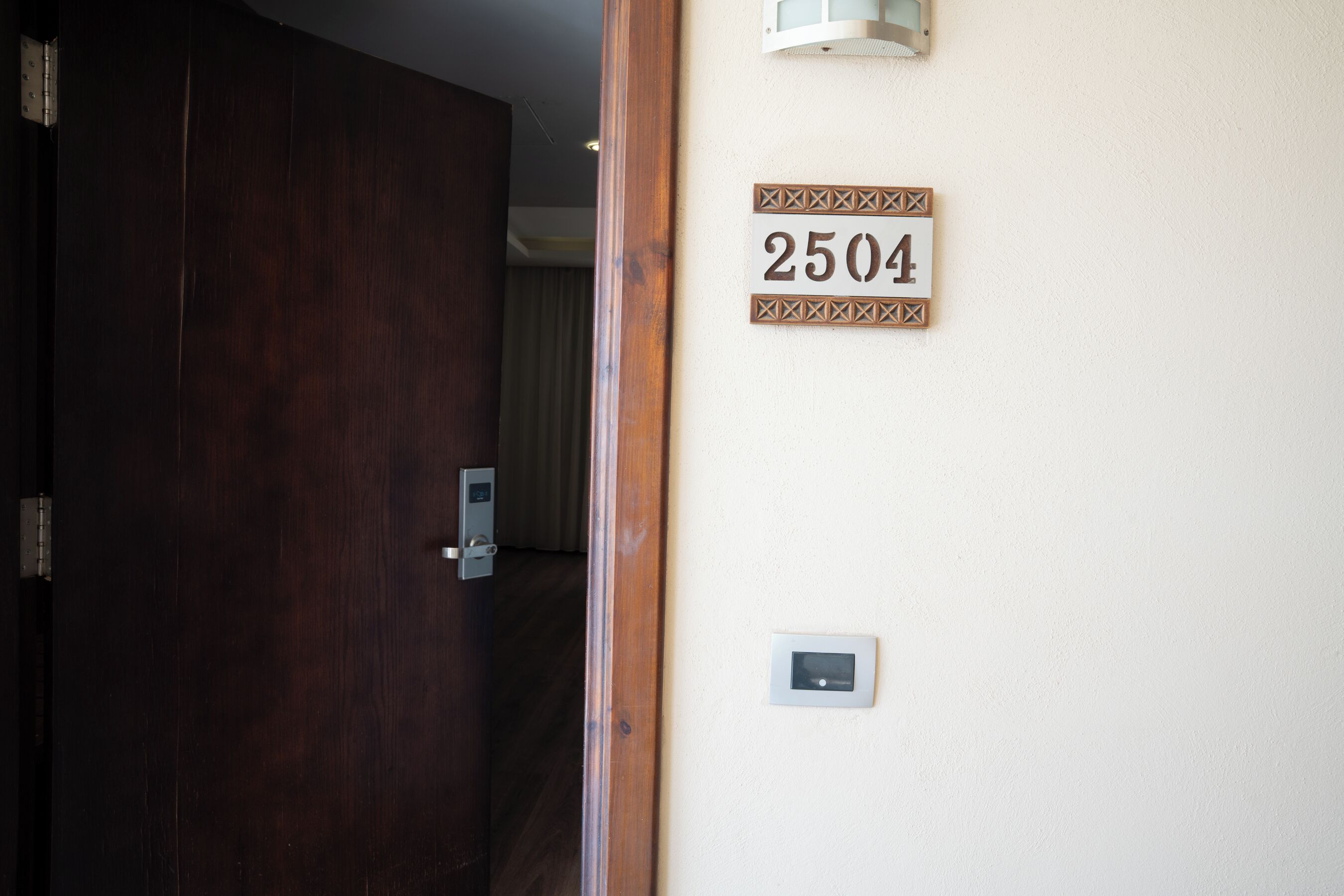 A hotel room entrance with a wooden door, a wall-mounted light fixture, and a room number sign.