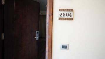 A hotel room entrance with a wooden door, a wall-mounted light fixture, and a room number sign.