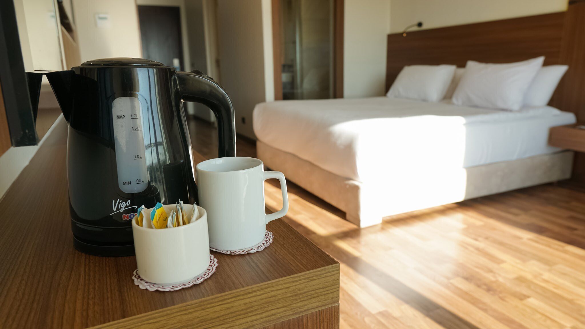 A hotel room with a bed, a coffee maker, and a mug on a wooden table.