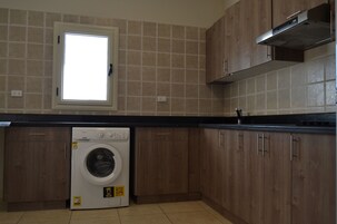 A laundry room with a washing machine, wooden cabinets, a window, and a tiled backsplash.