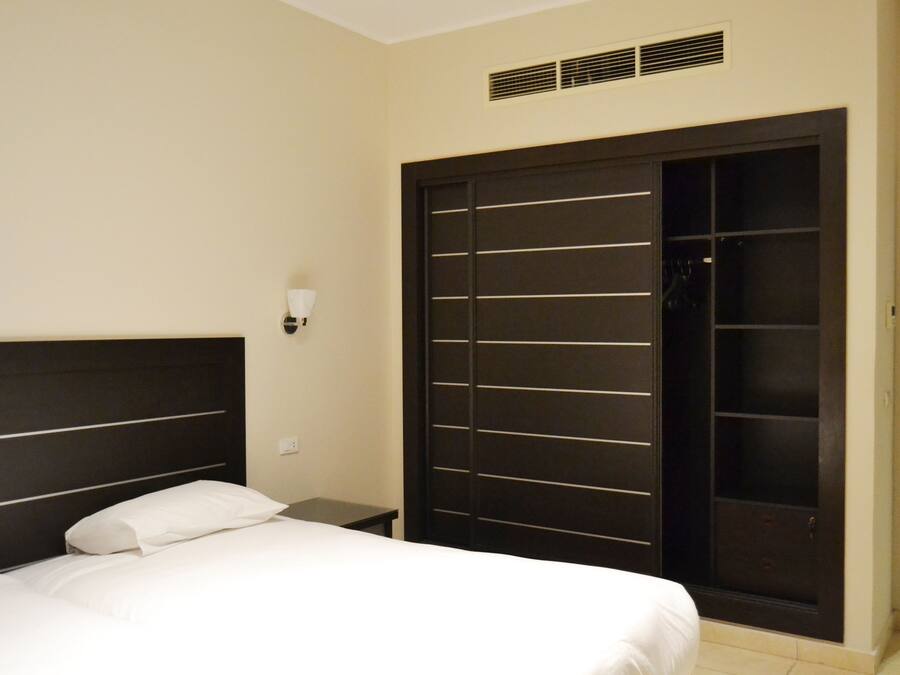 Un dormitorio con cama, mesita de noche, lámpara de pared y un armario amplio.