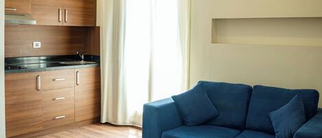 Una sala de estar moderna con un sofá azul, una mesa de centro de madera y una cocina con armarios de madera y encimera negra.