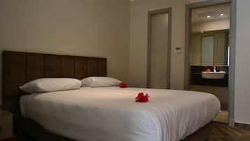 Een netjes opgemaakt bed met witte lakens en twee rode bloemen, een houten hoofdbord, en een badkamer met een wastafel en spiegel, zichtbaar door een open deur.
