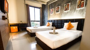 A hotel room with two beds, a desk, a TV, and artwork on the wall.