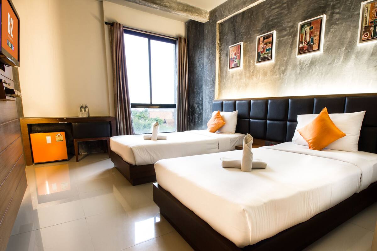 A hotel room with two beds, a desk, a TV, and artwork on the wall.