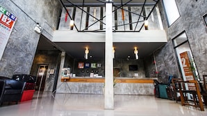 A hotel reception area with a marble wall, a reception desk, a cash register, and a staircase leading to an upper level.