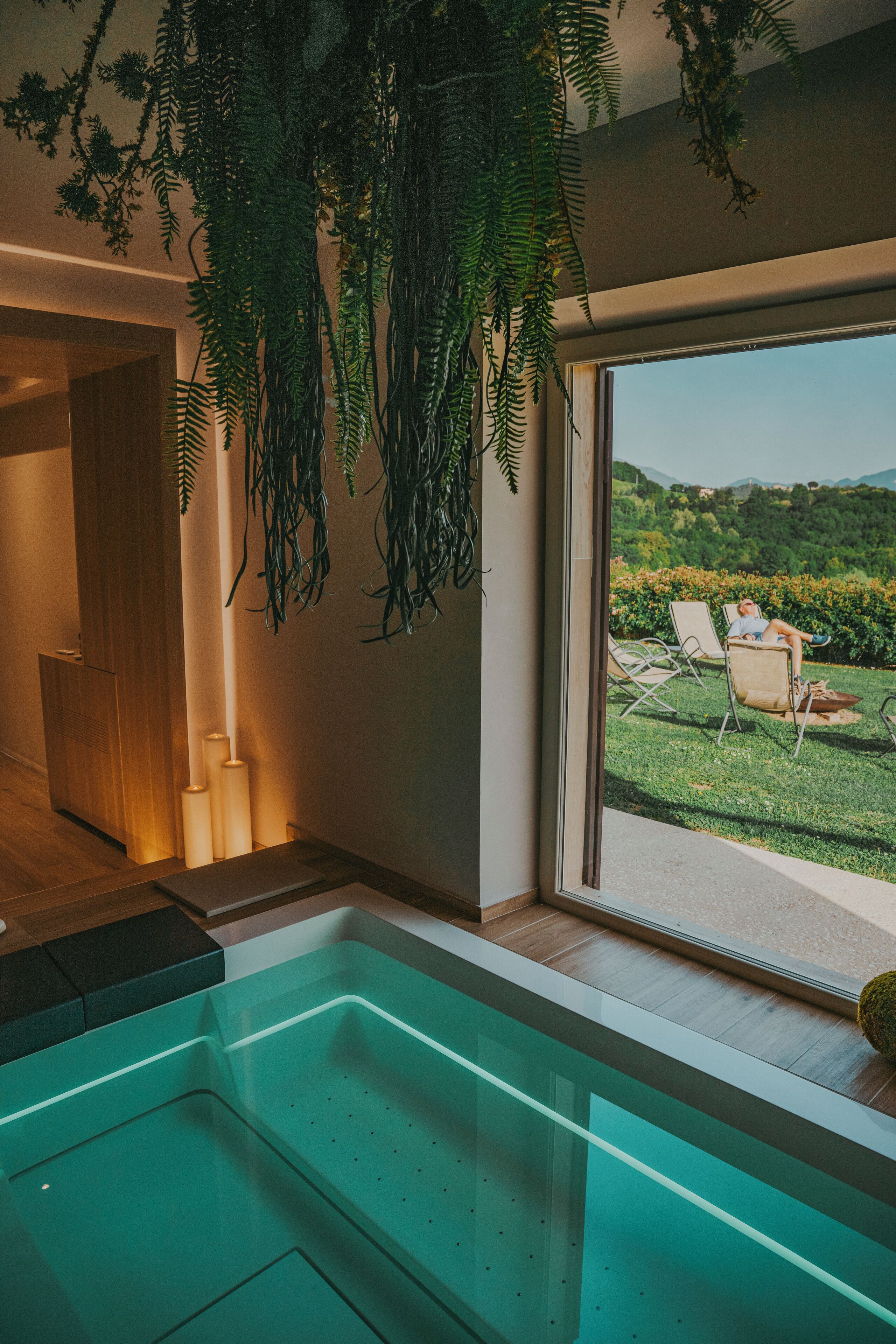 Une salle de bain moderne avec une douche à parois de verre, un plancher en bois et une vue sur un jardin et des collines.