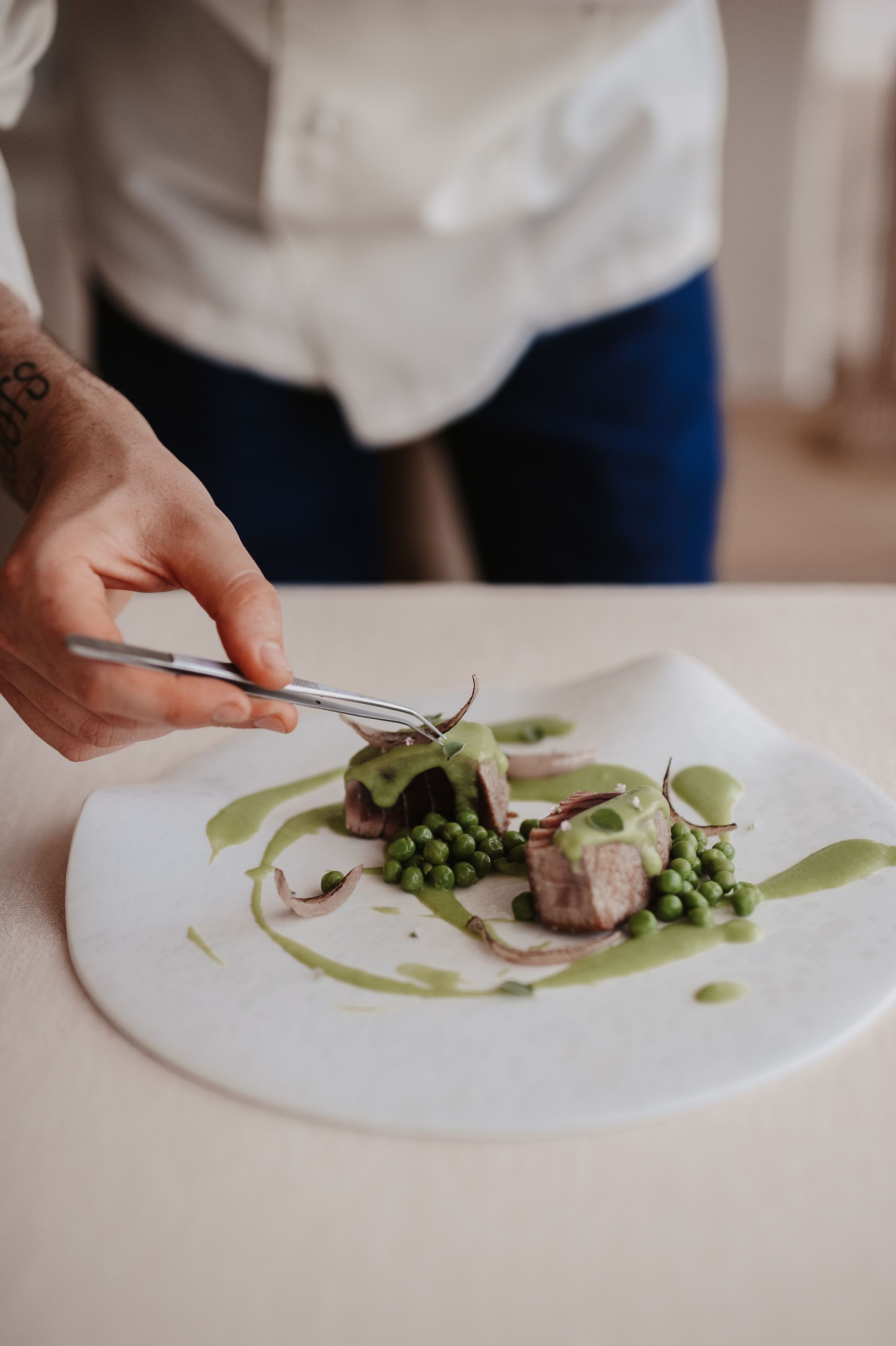 A person cutting a dish with green peas and sauce on a white plate.