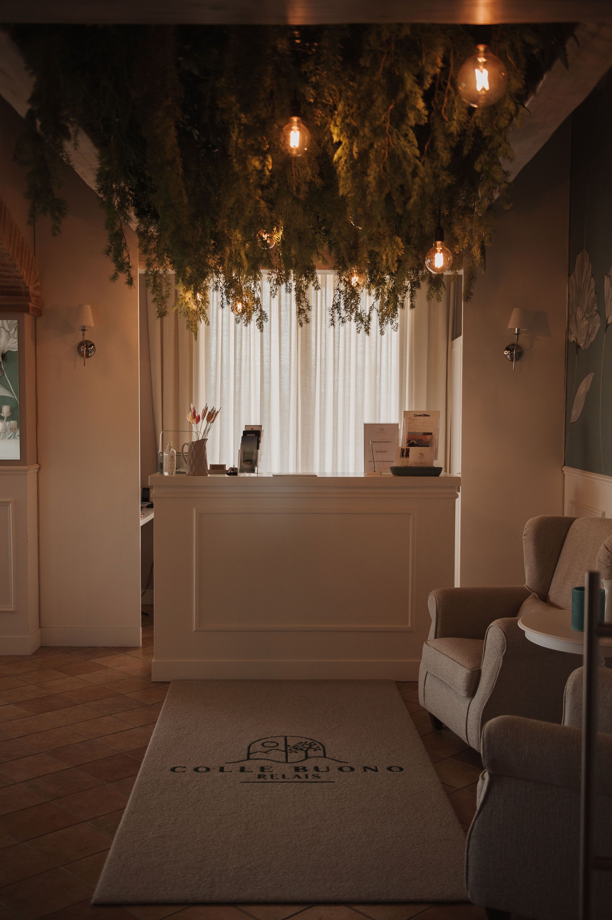 A reception area with a white reception desk, a grey armchair, and a doormat with "COLLE BUONO" text.