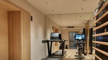 Un gimnasio moderno con cintas de correr, bicicletas estáticas y una pantalla de televisión.
