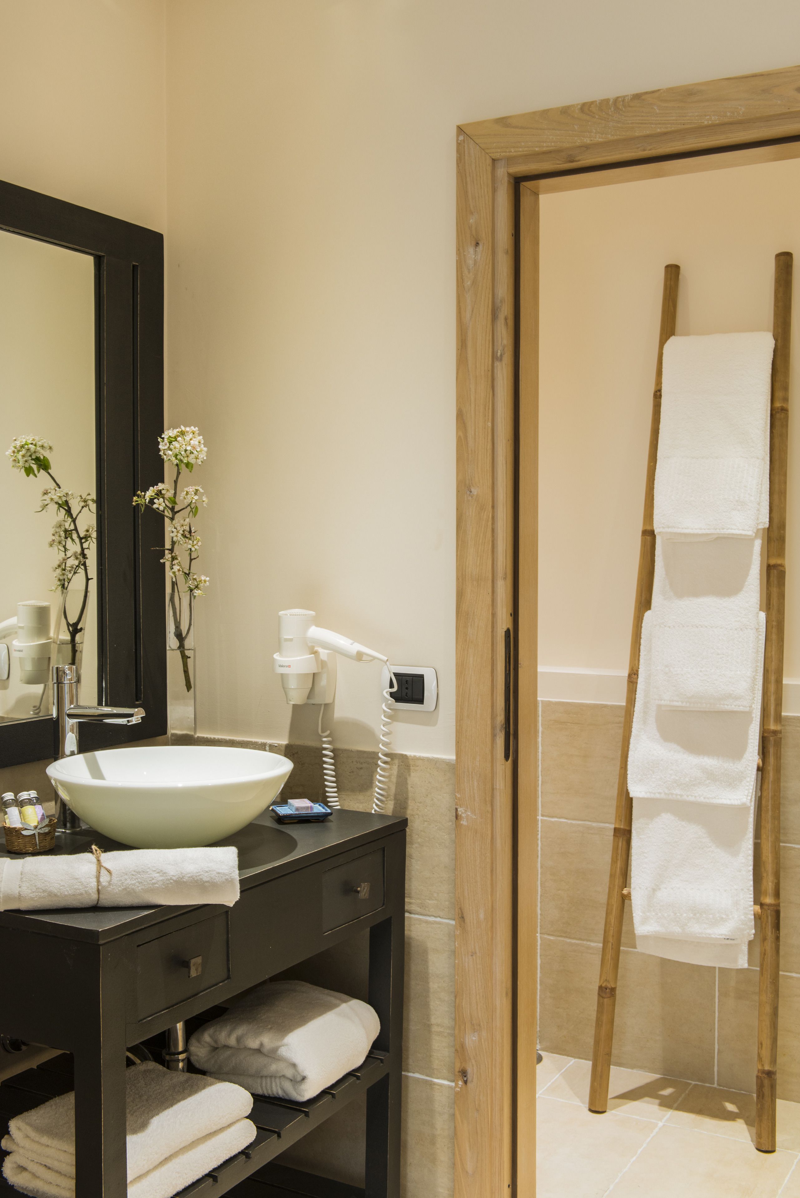 A bathroom with a large mirror, a white sink, a towel rack, and a wooden ladder.