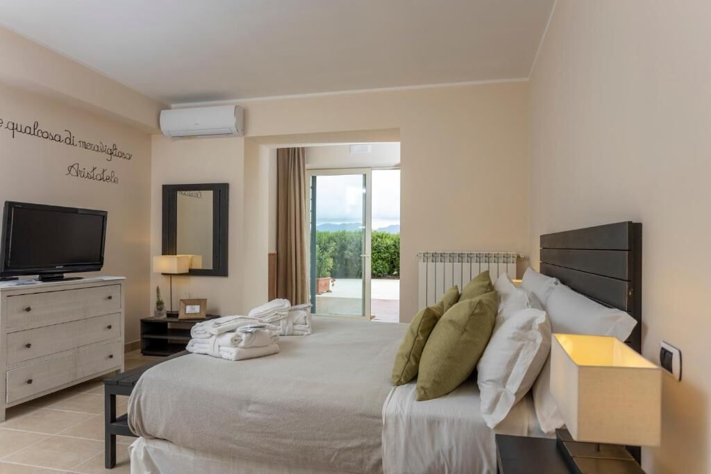 A hotel room with a bed, a TV, a dresser, a lamp, and a view of the outdoors.