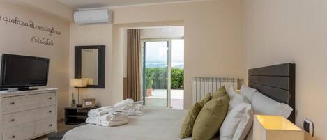 A hotel room with a bed, a TV, a dresser, a lamp, and a view of the outdoors.