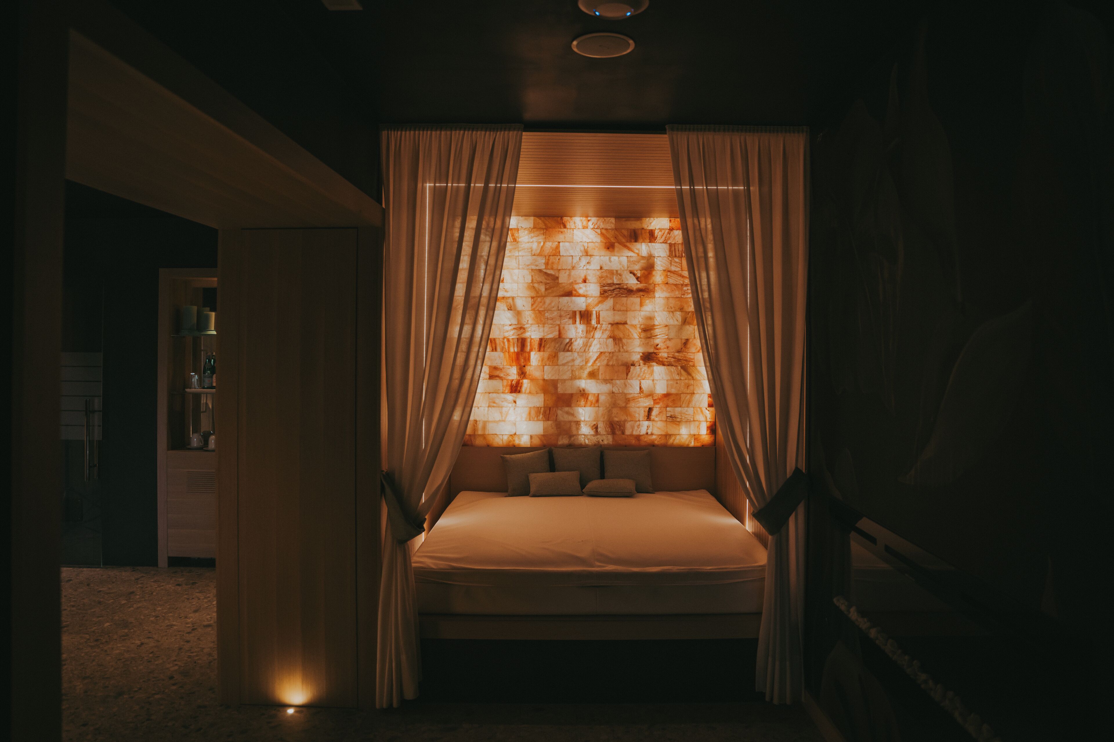 A dimly lit room with a bed, curtains, and a wall with a patterned design.